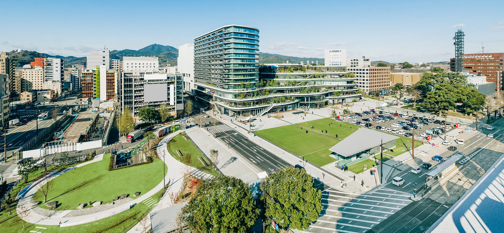 くまもと街なか広場(花畑広場)の全景。芝生広場の奥に緑のテラスをもつ建物が見える